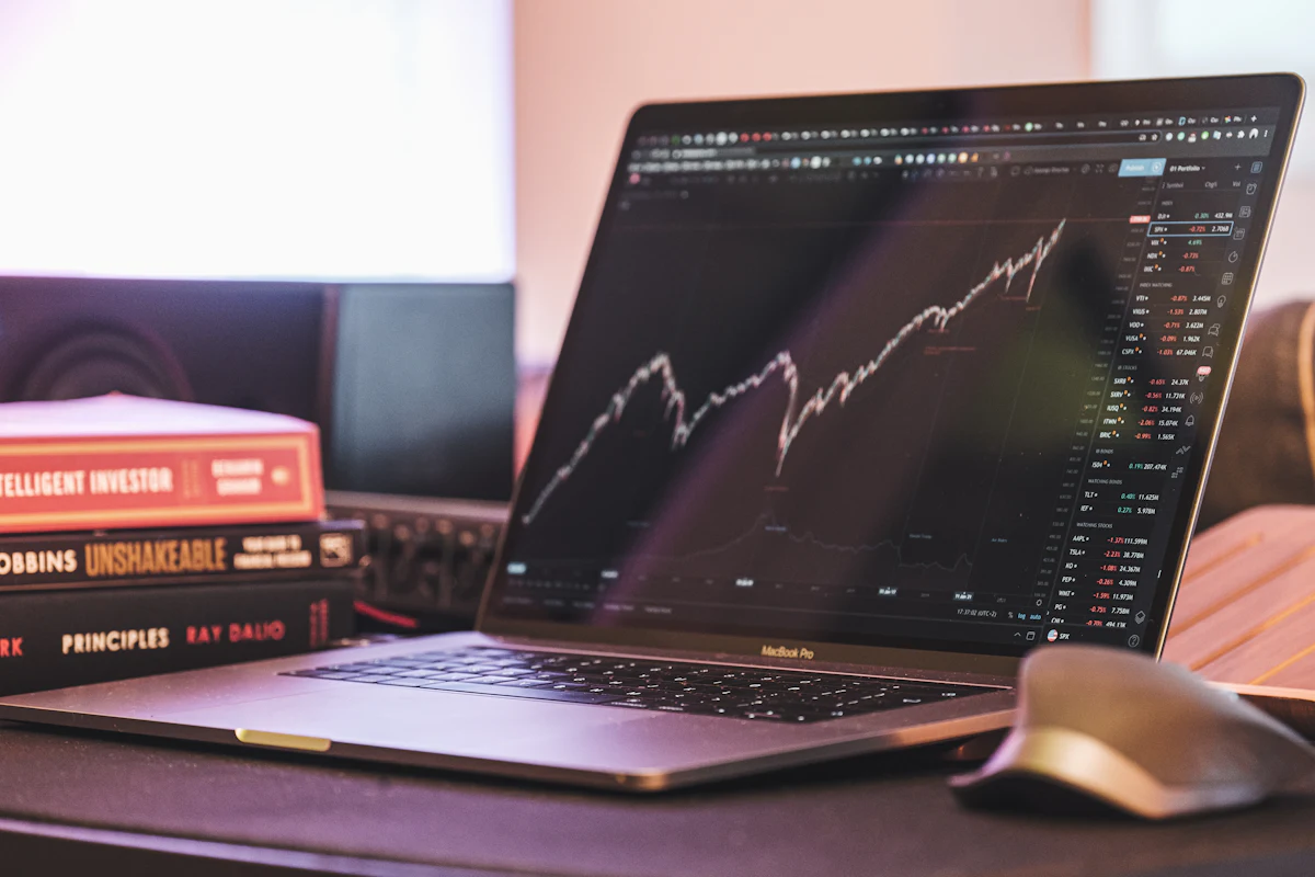 Laptop showing a rising stock index chart next to investing books