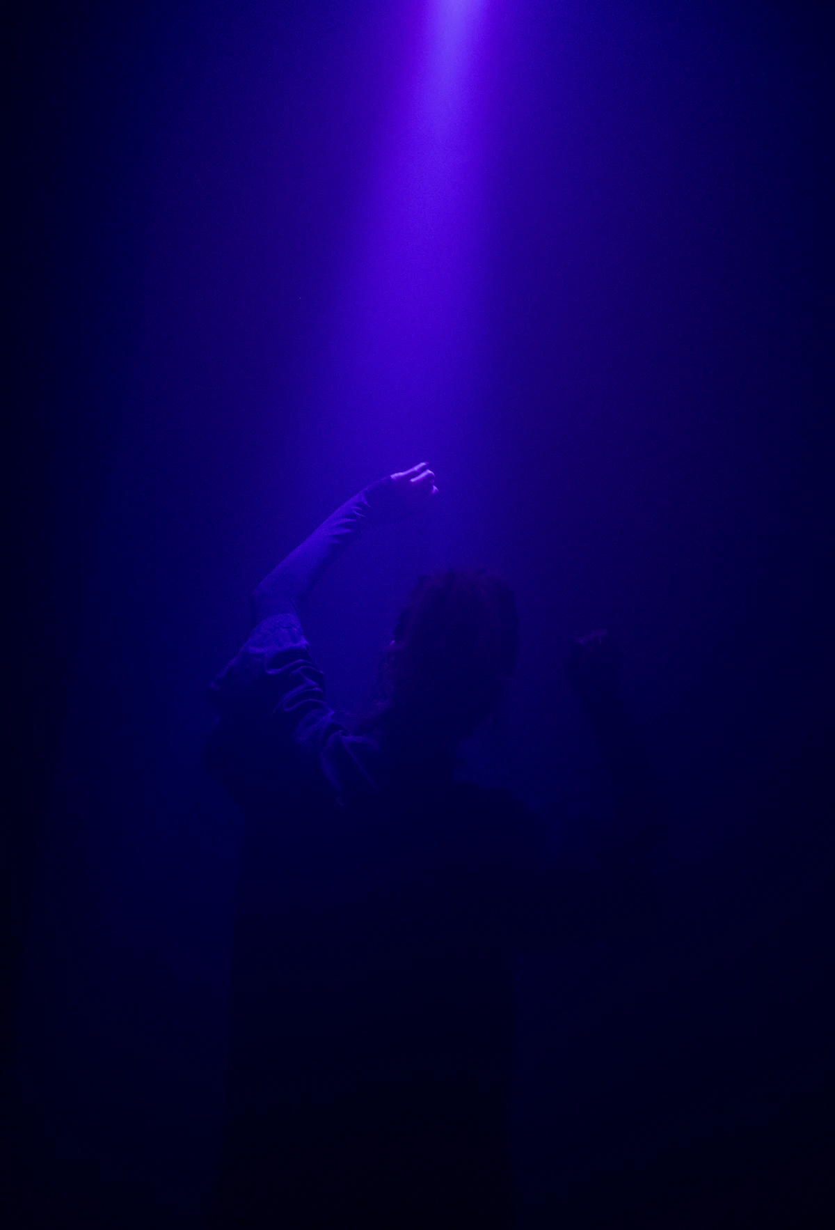 A lone figure reaching toward a single beam of light in the dark