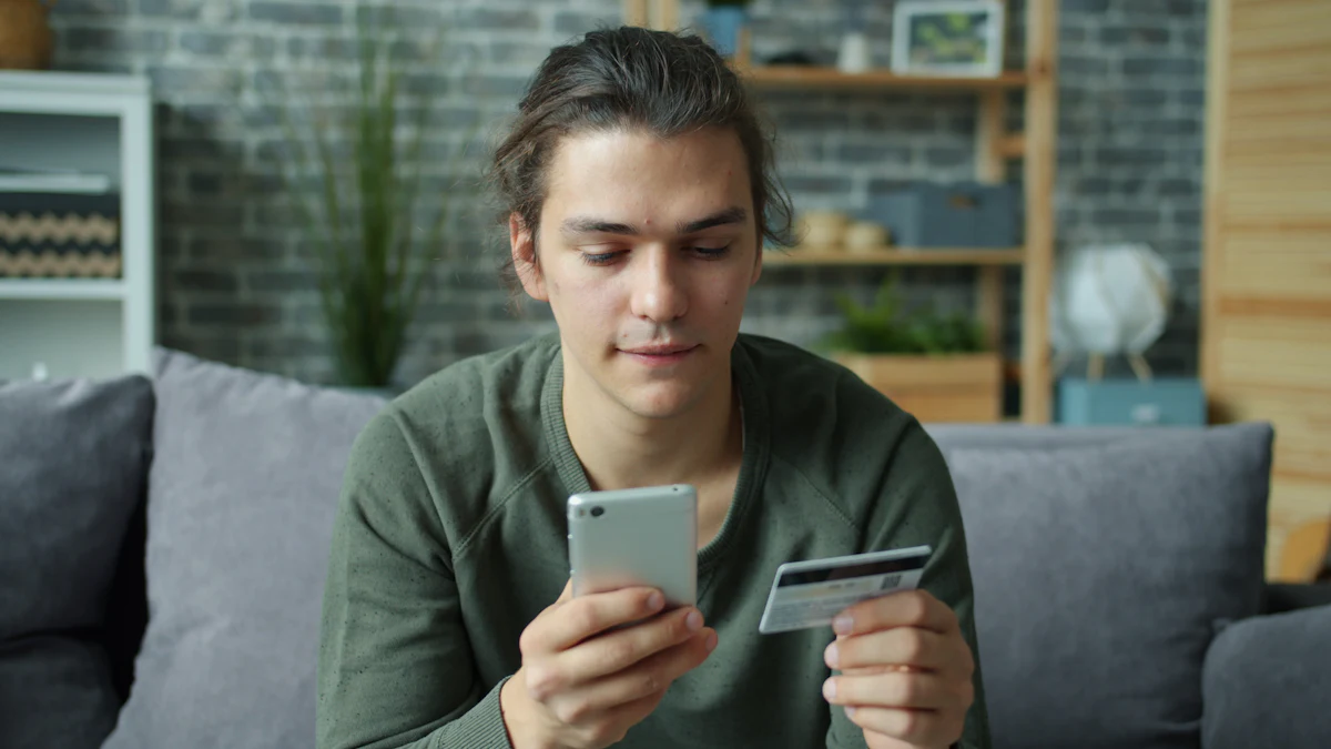 A young man sitting on a sofa using a smartphone while holding a credit card